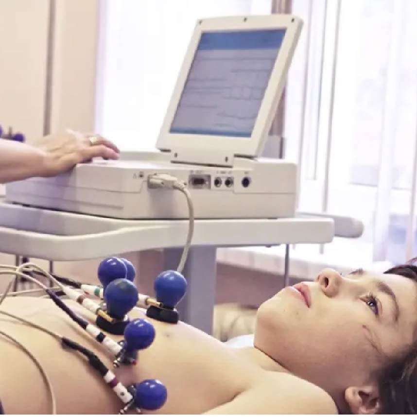 A boy lying on a bed, undergoing an EKG testing with a nurse monitoring him at a computer