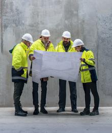 Four construction workers with hard hats looking at a plan