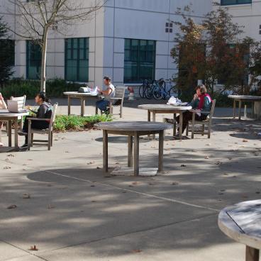 Diagonal front view of Schulz Building showing tables and chairs with some students seated